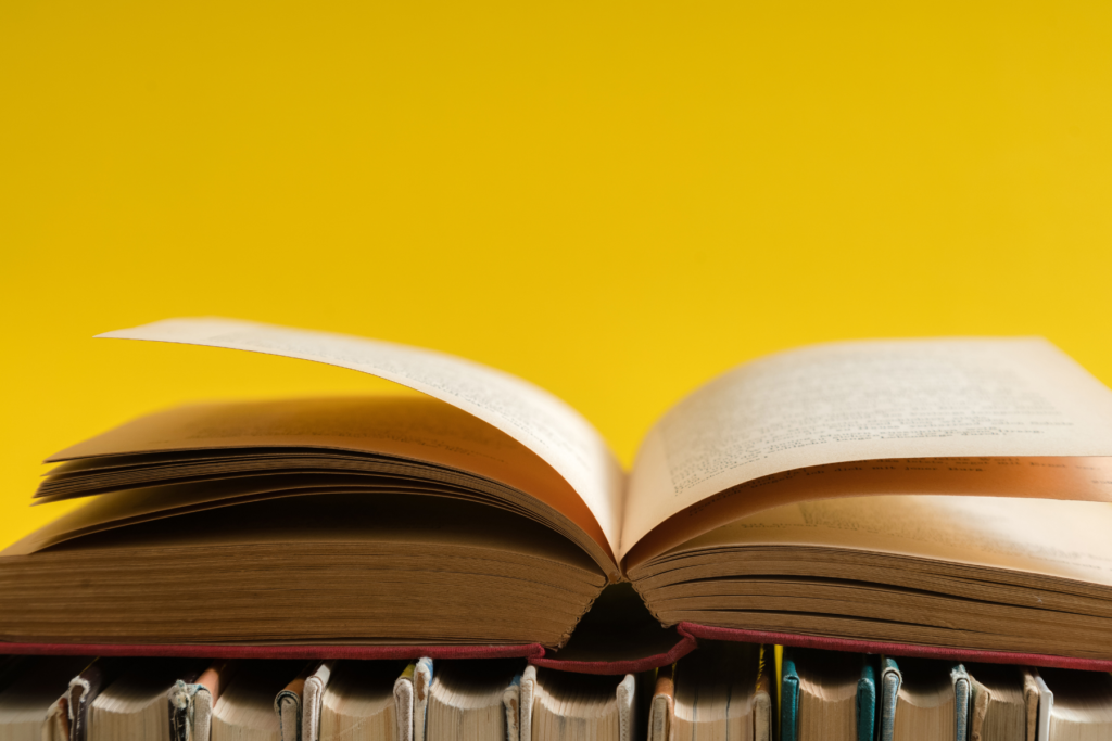 Livre ouvert sur une pile de livres, avec un fond jaune vif symbolisant la narration et la transmission du savoir